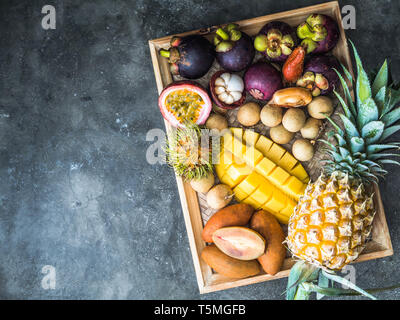 Various fresh Thai fruits - rambutan, mango, mangosteen, longan, sapodilla, passion fruit, salak, on a wooden tray and a gray background. Stock Photo