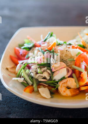 Traditional Thai cuisine. Rice noodle salad, fresh vegetables and herbs and seafood on a plate in a cafe. Authentic fresh traditional thai meal at the Stock Photo