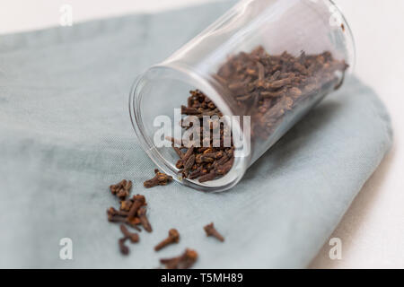 Closeup shot of cloves in transparent glass jar laying on a piece of linen. Stock Photo