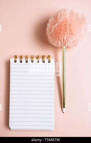 Top view of blank notebook with funny fluffy pen on pink pastel background with copy space, vertical composition Stock Photo