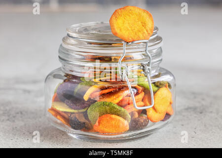 Colourful mix vegetable chips in glass jar on light gray background Stock Photo