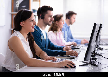Happy Young Customer Service Executives Using Earphones Working In Call Center Stock Photo