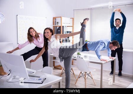 Smiling Young Businesspeople Doing Yoga In Office Stock Photo