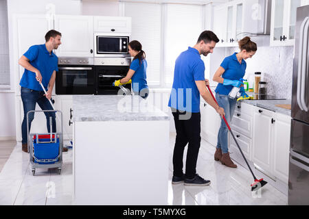 Group Of Young Janitors In Uniform Cleaning Kitchen At Home Stock Photo