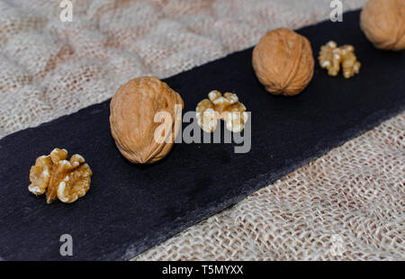 Walnuts, with and without shell, on black table surface, over sack texture Stock Photo