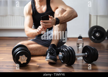 Man Sitting On Hardwood Floor In Gym Using Smartphone Stock Photo