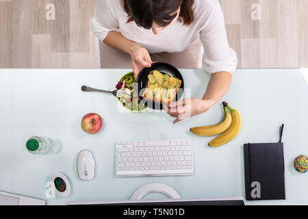 An Overhead View Of Businessperson's Hand Eating Salad With Fork On Desk Stock Photo