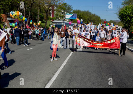 Russia, Nakhodka, 05/09/2017. Cute young lady does selfie in front of big red banner with inscription 'Immortal Regiment'. Annual event Immortal Regim Stock Photo