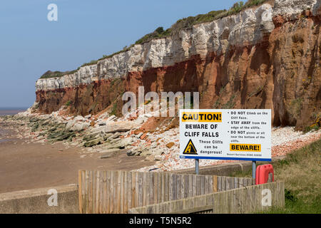 Warning sign of cliff falls at Hunstanton cliffs Norfolk UK with peeple sitting under cliffs in the dangerous area Stock Photo