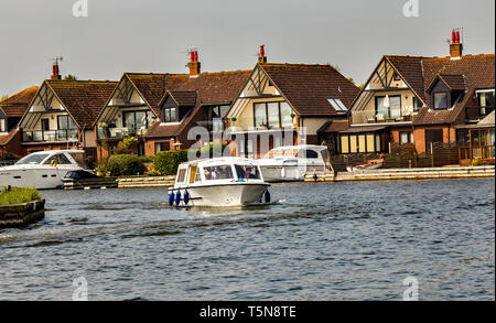 Small hire boat navigating the River Bure in Horning, a village in the heart of the Norfolk Broads. This section is on route to the Swan Inn and passe Stock Photo