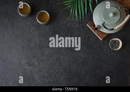 Teapot and Teacups on black background, copy space. Traditional Asian Tea Set -  iron teapot and ceramic teacups with green tea for tea ceremony. Stock Photo