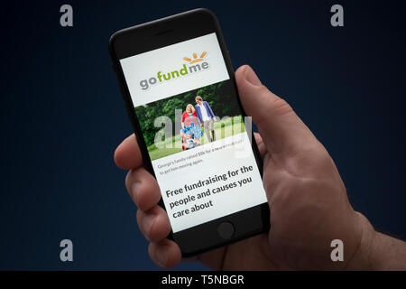 A man looks at his iPhone which displays the Go Fund Me logo (Editorial use only). Stock Photo