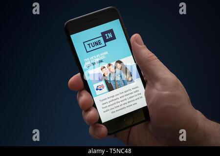 A man looks at his iPhone which displays the Tune In logo (Editorial use only). Stock Photo