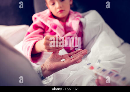 Girl in pink bathrobe taking pills from granny while feeling sick Stock Photo