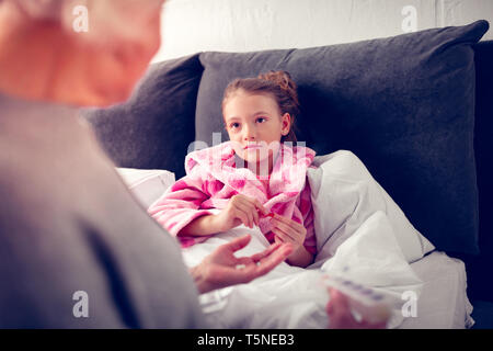 Girl staying in bed while feeling sick and looking at granny Stock Photo