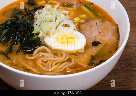 Ramen miso of Meat with pork, soy milk, pork broth, black mushrooms, eggs, onions, corn, carrots and courgettes served in a bowl, dark wooden table ba Stock Photo
