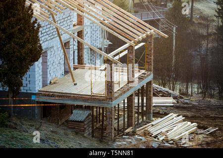 Cottage house building under construction with walls made of hollow foam insulation blocks, wooden roof frame and attached porch terrace with brick co Stock Photo