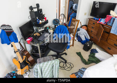 Messy, cluttered teenage boys bedroom with untidy piles of clothes, electronics, music and sports equipment. Stock Photo