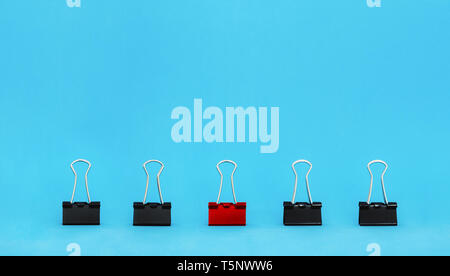 Unique, leadership, individuality, and think different concept. Office supplies, red binder paper clip stand out of other clips Stock Photo