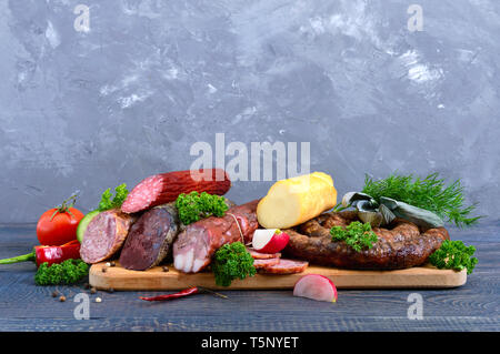 Many kinds of sausage, smoked cheese, fresh vegetables on a wooden background. Products to the holiday. Stock Photo