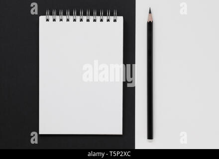 Blank white notepad and black pencil, on a black and white background. Flat lay with copy space. Stock Photo