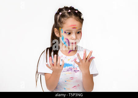 scared little child girl looks at his hands painted in colorful paint isolated on white background. Stock Photo