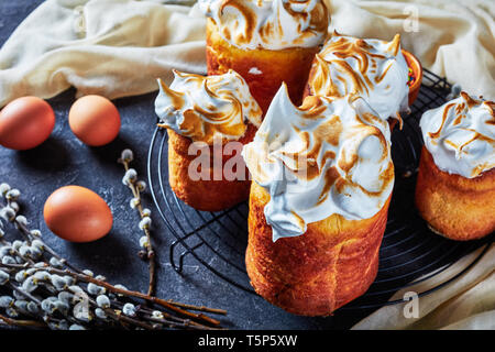 delicious sweet easter bread, panettone topped with whipped egg whites on a wire rack on a concrete table with cloth eggs and willow twigs, horizontal Stock Photo