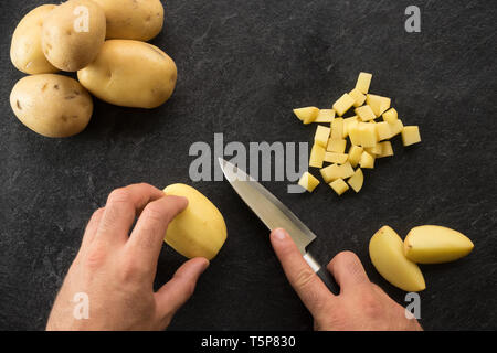 Hand cutting potatoes on textured black background. Photo from above Stock Photo
