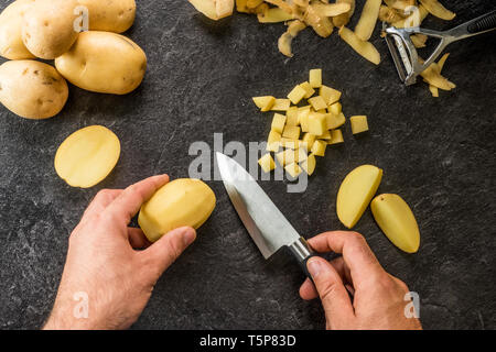Hand cutting potatoes on textured black background. Photo from above Stock Photo