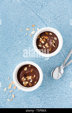 Dark chocolate dessert in two ceramic ramekins and spoons on blue textured and patterned background. Top view and space for text. Stock Photo