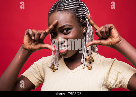 Funny girl makes frame of the fingers near the face. Photo of african girl with perfect skin on red background. Stock Photo