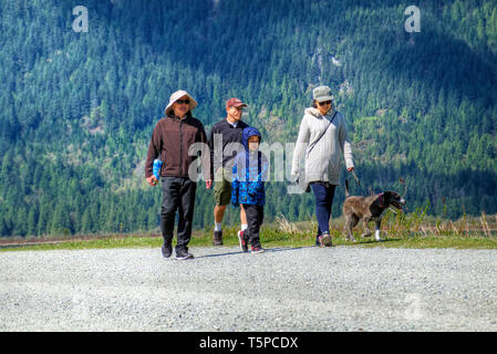 Small group of people with a dog walking along a dike beside the Pitt River in Pitt Meadows, B. C., Canada Stock Photo