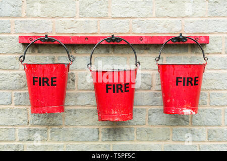 Three red fire buckets hanging on a brick wall filled with water Stock Photo