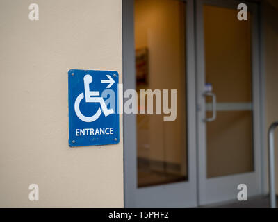 Handicap entrance sign pointing to right in front of office door Stock Photo