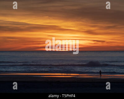 Man watches waves over ocean with sun setting during dusk hours Stock Photo