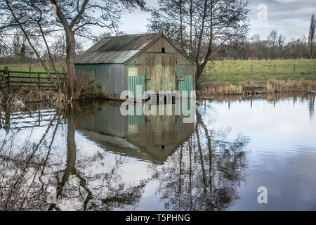 An old corrugated tin boat house with reflection in the water of Wedgwood pool near Barlaston, Stoke on Trent, UK. Stock Photo