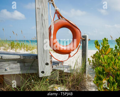 Bright orange life bouy hanging on side of beach access on tropical island close up. Stock Photo