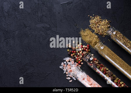 Different spices and salt in glass tubes on dark stone background with copy space Stock Photo