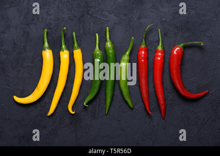 Different colored chilli peppers sorted by color on dark stone background Stock Photo