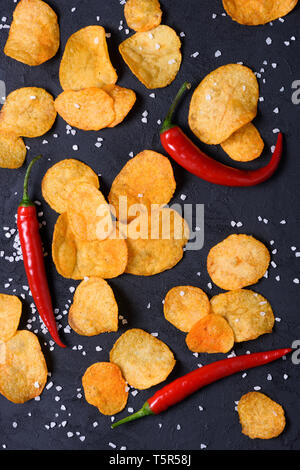 Potato chips with salt and chilli pepper on dark stone background Stock Photo