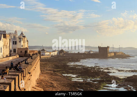 View of Essaouira at sunset. The old part of town is the UNESCO world heritage sites.  Tourists and locals are enjoying the sunset at the old walls of Stock Photo