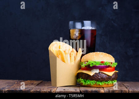 Burger fries and glass of soft cold drink with ice on wooden table with blank black chalkboard on background Stock Photo