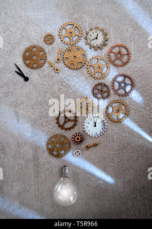 Clock parts including hands gears and cogs in the shape of a question mark with light bulb Stock Photo