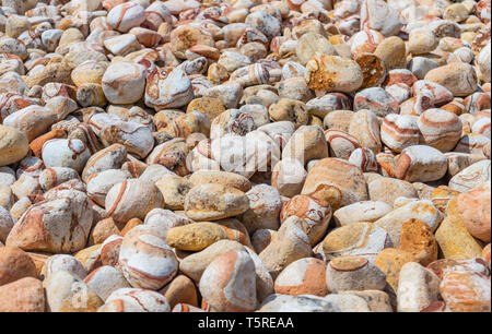 Natural pebbles background, Smooth round stones beige yellow color piled up outdoors, sunny day Stock Photo