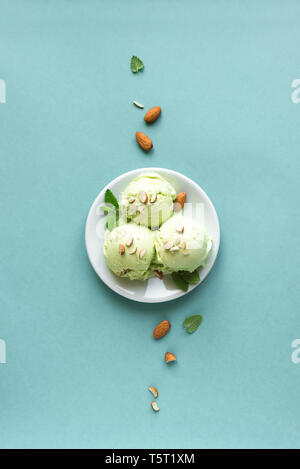 Green Ice Cream on blue background, top view, copy space. Green pistachio, avocado or green tea gelato with almonds and mint leaves. Stock Photo