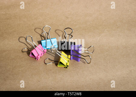 Clips for paper of different colors on the background of rough brown kraft paper. Stationery. With copy space for text. Stock Photo