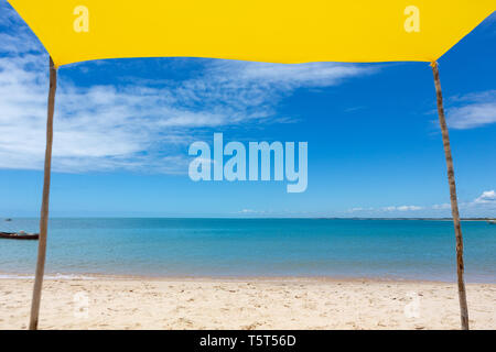 Beautiful beach view from inside yellow tent on sunny summer day. Sea and blue sky in the background. Concept of vacations, peace and relaxation.Bahia