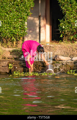 Vertical portrait of a lady doing the washing up on the riverbank in Alleppy, India Stock Photo