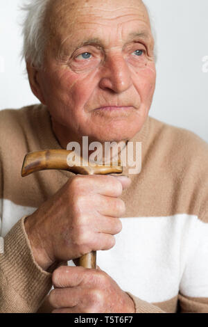 Portrait of an old sad man who put his head on the handle of a wooden cane, the concept of loneliness at home. Stock Photo
