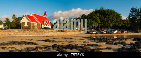 A panorama of the famous red church at Cap Malheureux on the island of Mauritius with people working on fisher boats.. Stock Photo